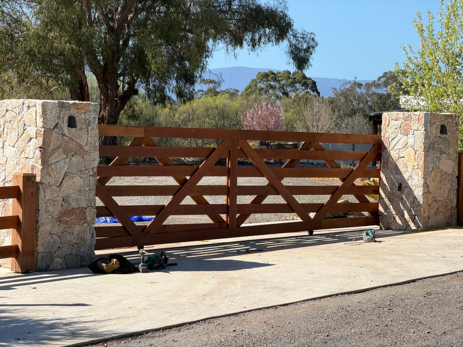 Custom braced timber driveway gate hung between stone pillars