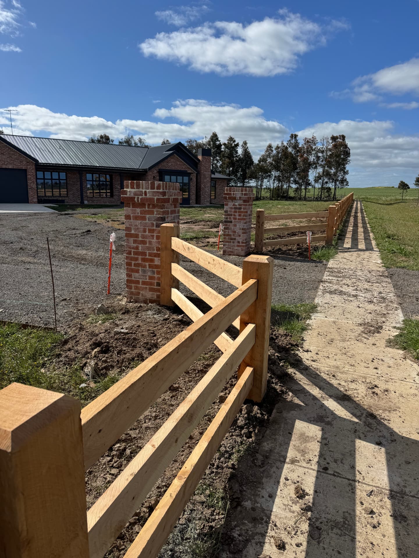 New post and rail fence line running past brick entrance piers